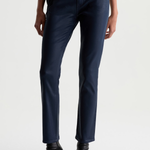 A person wearing dark navy slim-fit jeans with black pointed-toe ankle boots, shown from the waist down against a plain light gray studio background.