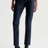 A person wearing dark navy slim-fit jeans with black pointed-toe ankle boots, shown from the waist down against a plain light gray studio background.