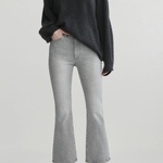 A model wearing a dark charcoal gray knit sweater, light gray cropped flare jeans, and black pointed-toe heels, standing against a light gray studio background.