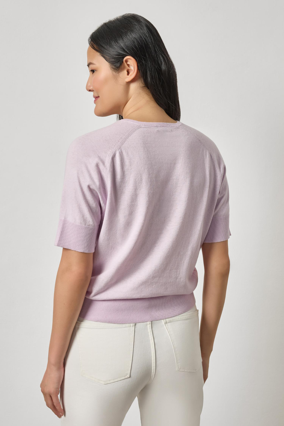 Woman wearing a light purple sweater and white pants on a plain background