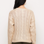 A woman viewed from the back wearing a cream cable-knit sweater and dark olive pants against a plain white background.