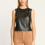 A woman modeling a sleeveless black faux-leather top paired with tan pants, shot against a plain light background.