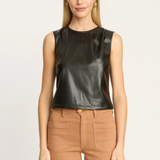 A woman modeling a sleeveless black faux-leather top paired with tan pants, shot against a plain light background.