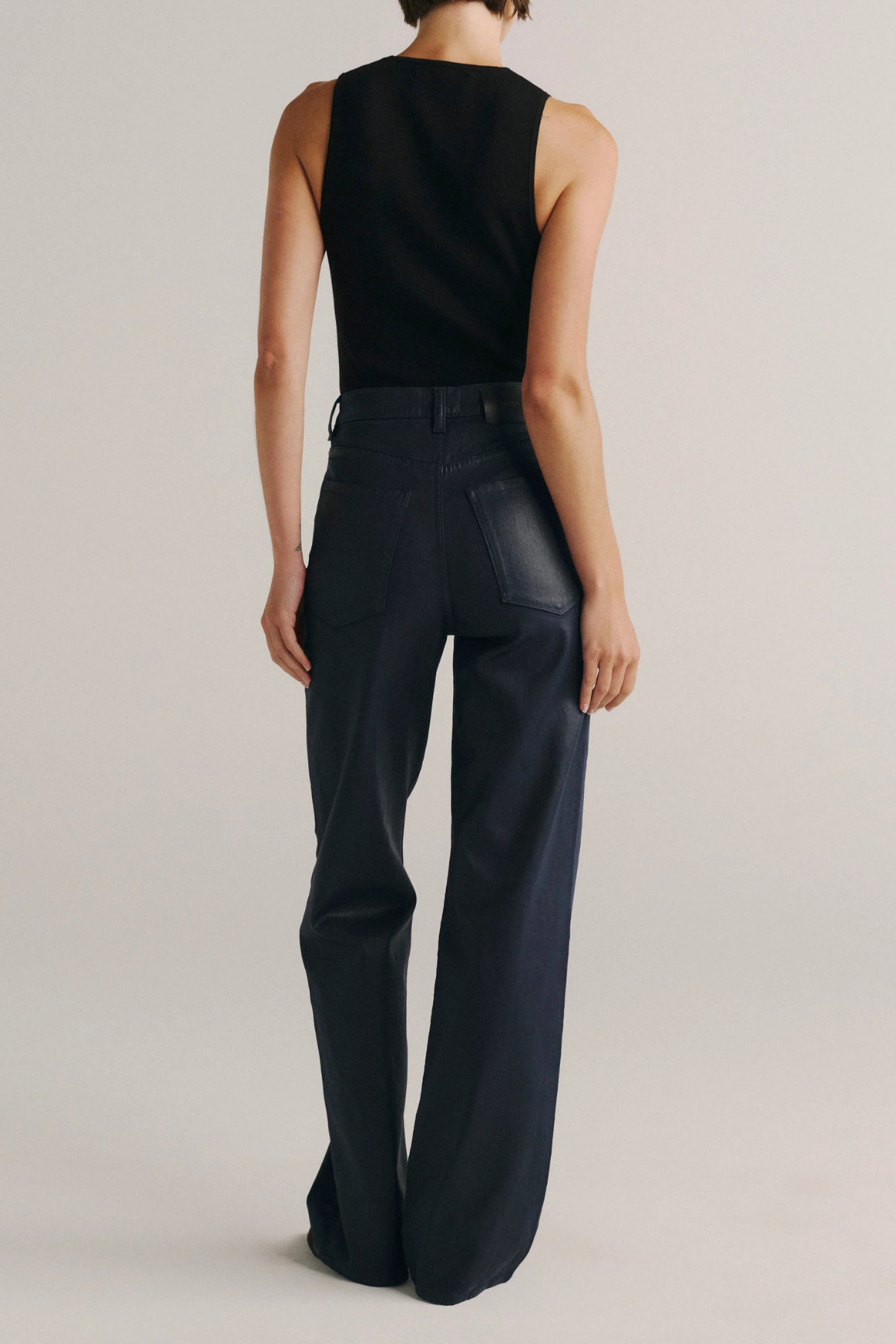 A model shown from the back wearing a black sleeveless top and dark navy wide-leg trousers against a light gray studio background.