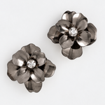 A pair of dark metallic flower-shaped earrings with a clear rhinestone center, displayed on a clean white background.