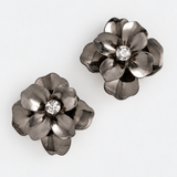 A pair of dark metallic flower-shaped earrings with a clear rhinestone center, displayed on a clean white background.