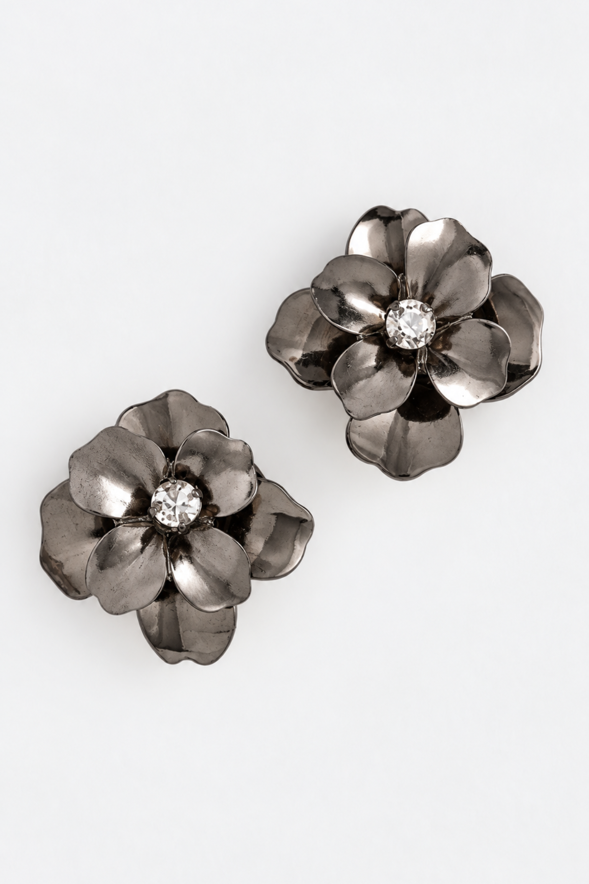 A pair of dark metallic flower-shaped earrings with a clear rhinestone center, displayed on a clean white background.