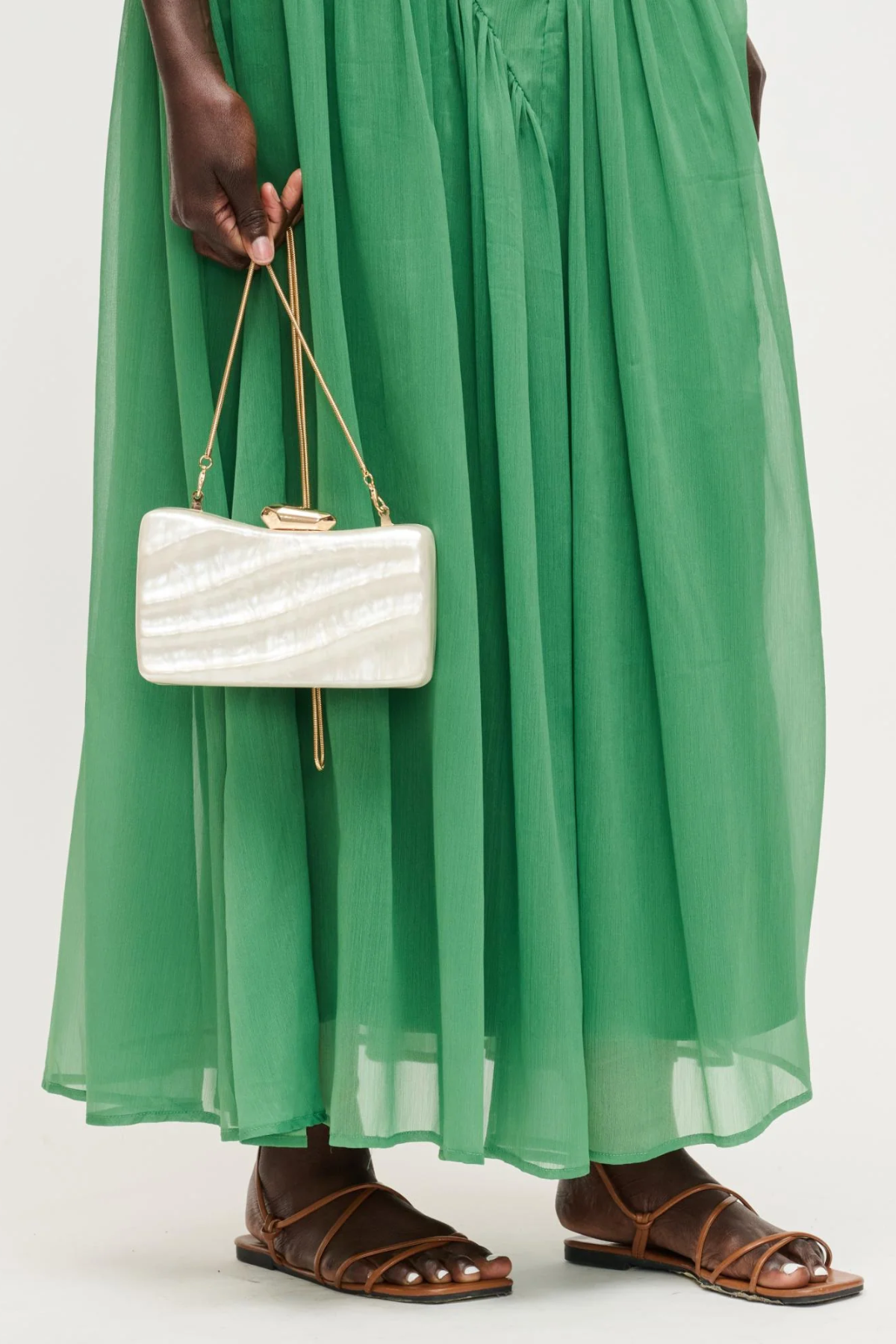 Person wearing a green dress holding a white handbag with gold handle on a white background