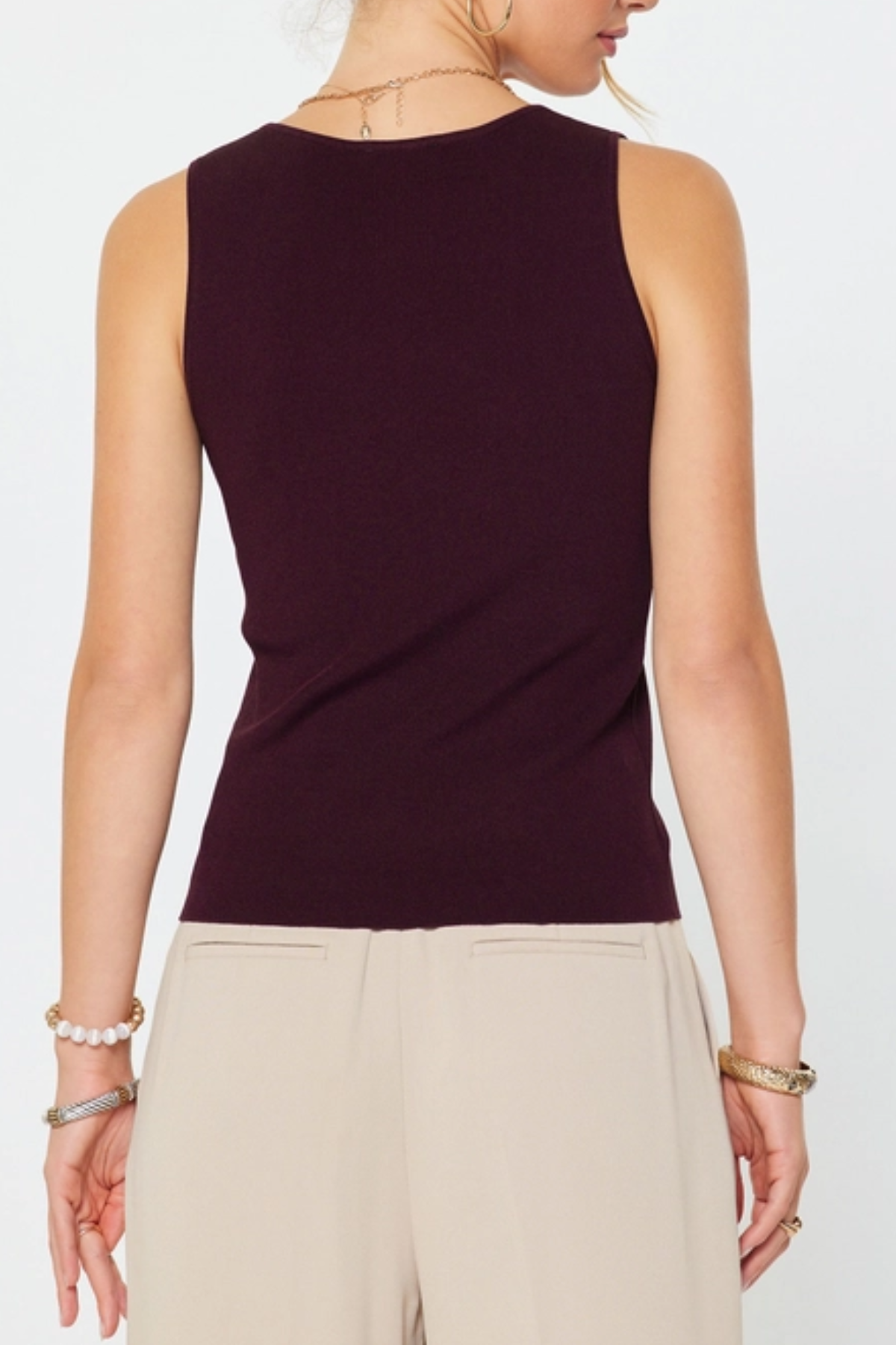 Person wearing a dark purple sleeveless top and beige pants on a white background