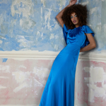 Woman in a blue dress standing against a textured wall.