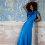 Woman in a blue dress standing against a textured wall.
