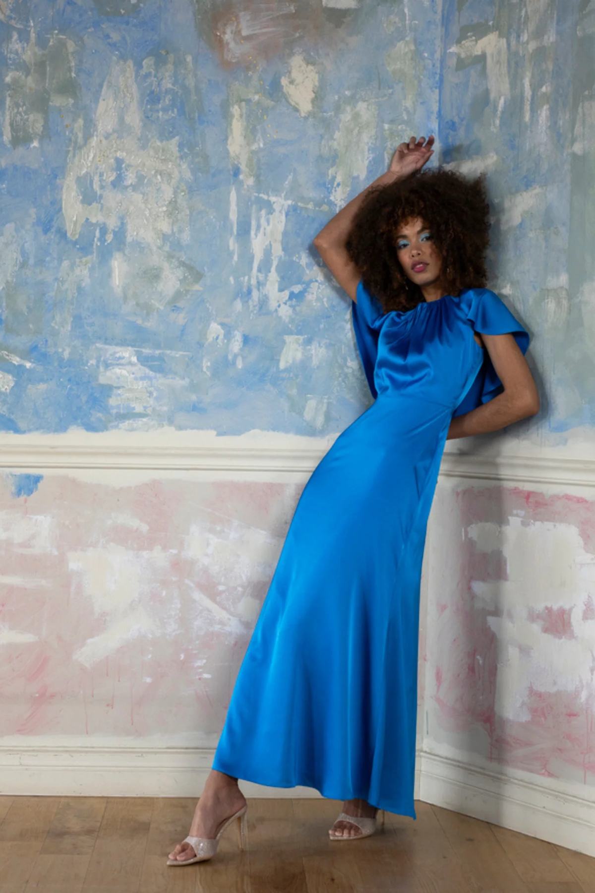 Woman in a blue dress standing against a textured wall.