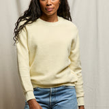 Woman wearing a light yellow sweater and blue jeans against a neutral background