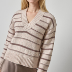 Woman wearing a beige and brown striped sweater against a plain background