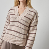 Woman wearing a beige and brown striped sweater against a plain background