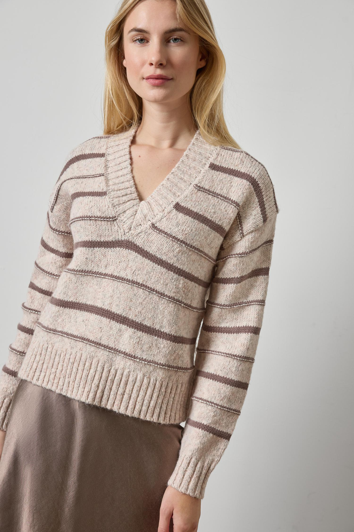 Woman wearing a beige and brown striped sweater against a plain background