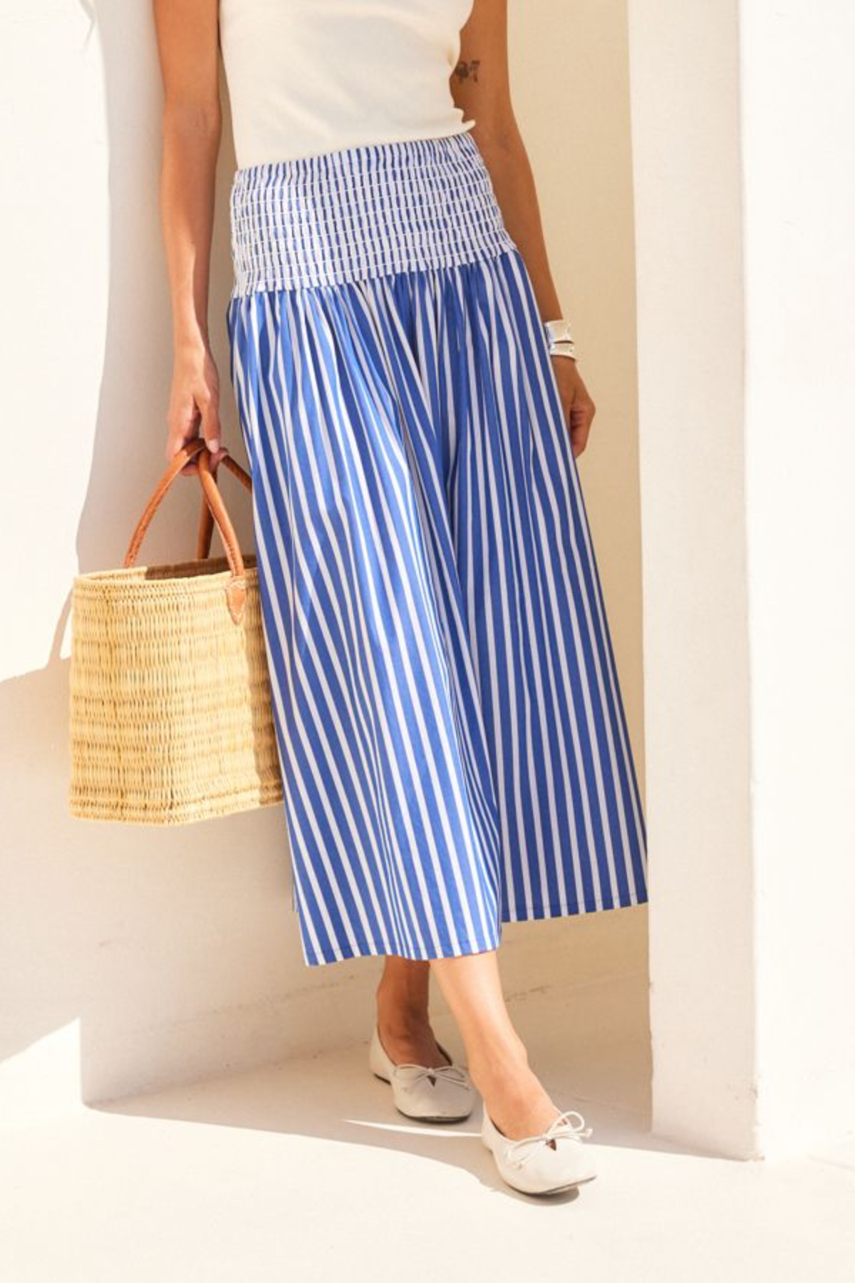 Person wearing a blue and white striped skirt holding a straw bag indoors.