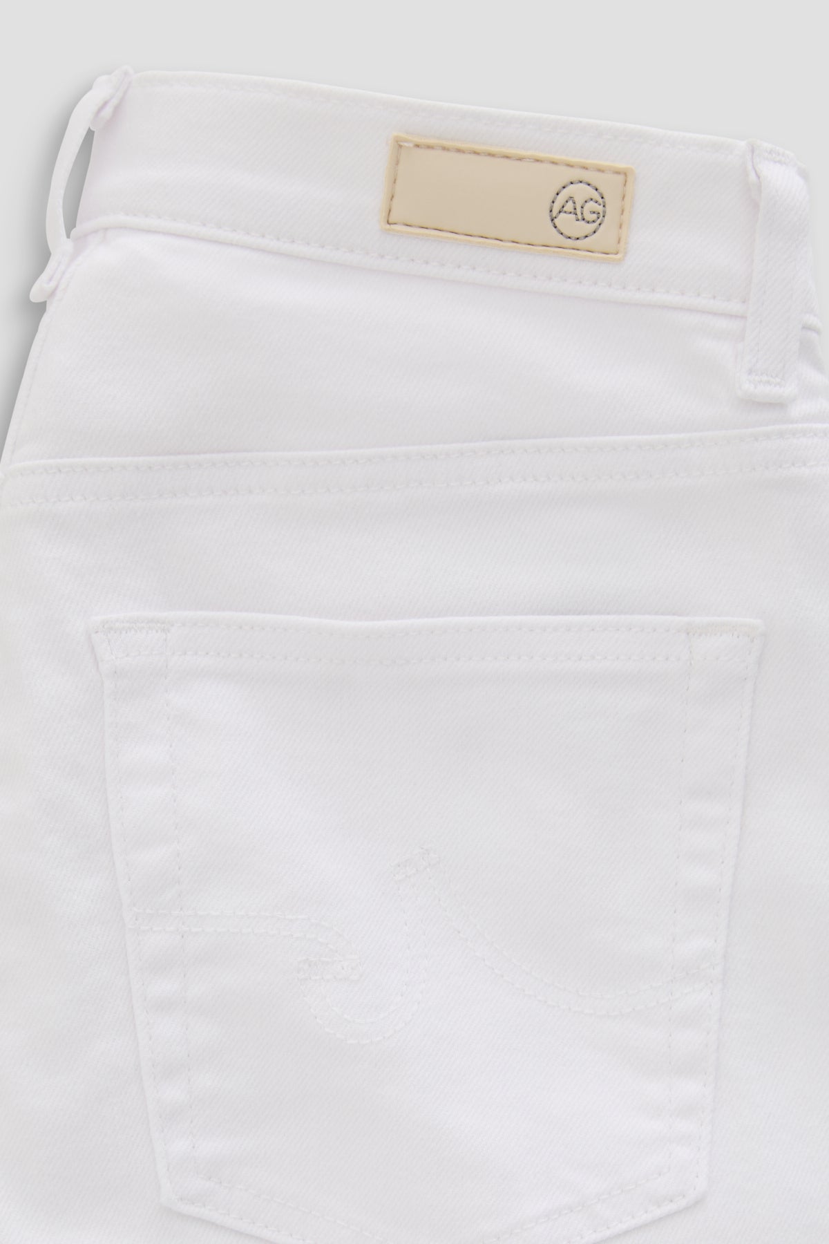 Close-up of the back waistband and pocket area of white denim jeans, showing a beige brand patch with a circular logo.