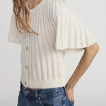 Woman wearing a white ribbed blouse with short sleeves and blue jeans on a plain background