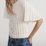 Woman wearing a white ribbed blouse with short sleeves and blue jeans on a plain background