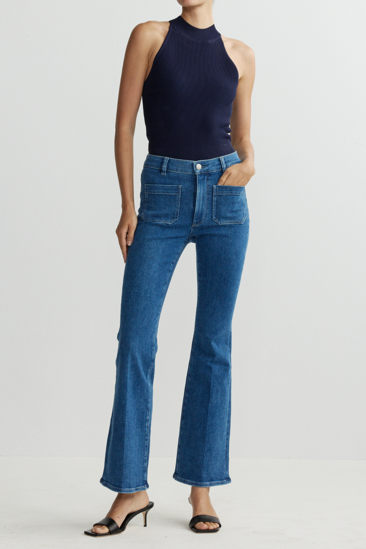 Person wearing a navy sleeveless top and blue jeans on a light gray background