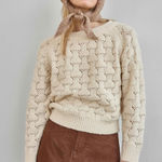 Person wearing a beige knitted sweater with a hood against a plain background