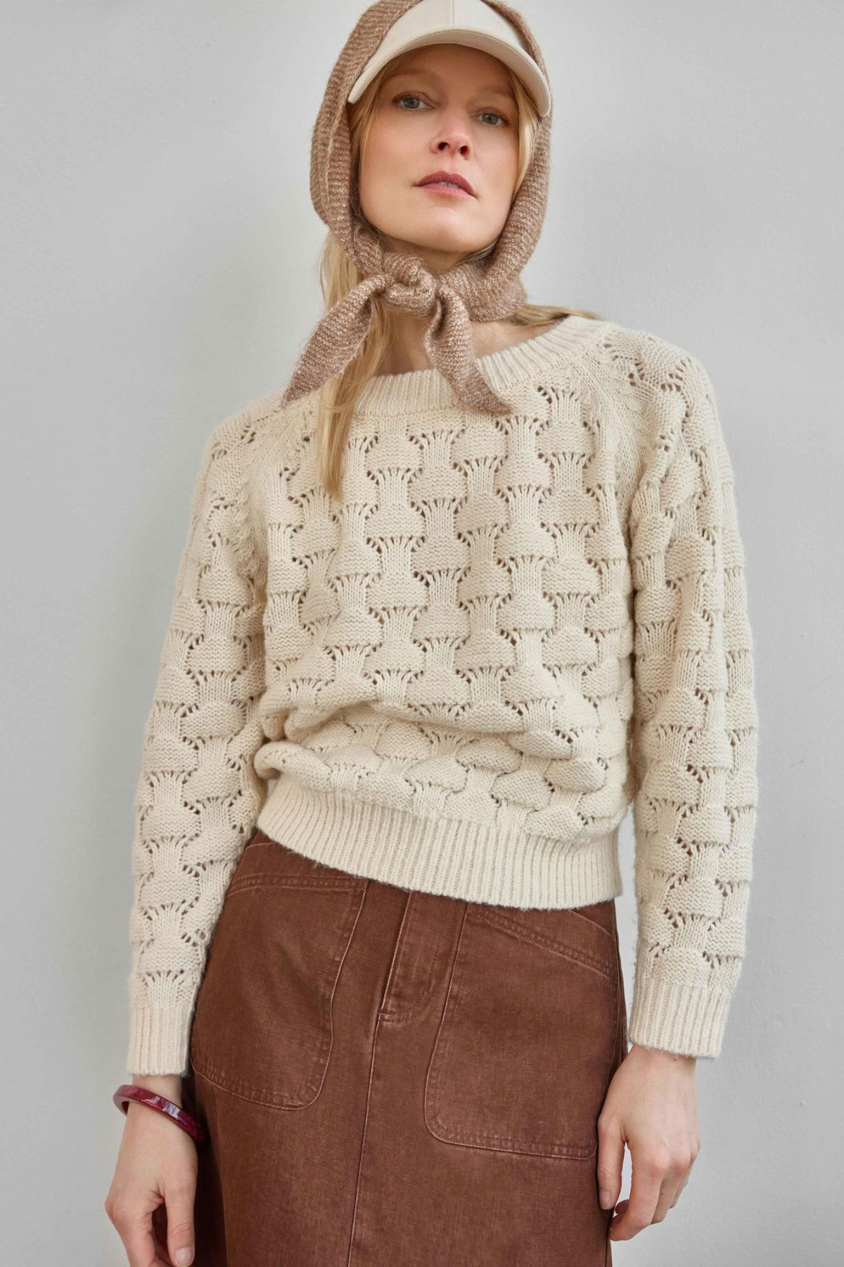 Person wearing a beige knitted sweater with a hood against a plain background