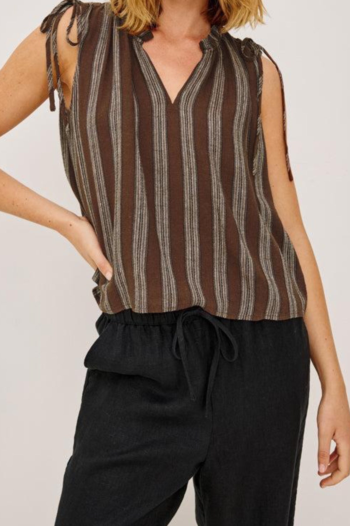 Person wearing a brown striped sleeveless top and black pants on a plain background