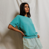 Woman wearing a teal sweater and striped skirt against a plain background