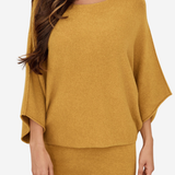A woman wearing a mustard yellow knit two-piece set consisting of a wide-sleeve top and matching pants, shown against a plain light gray background.