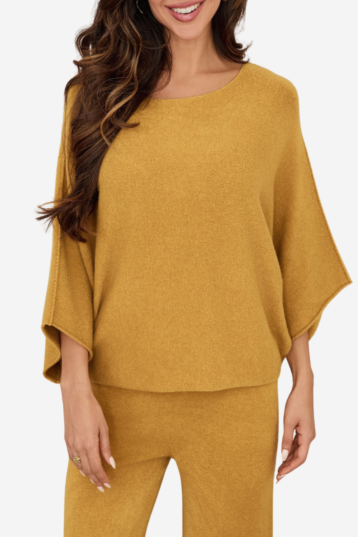 A woman wearing a mustard yellow knit two-piece set consisting of a wide-sleeve top and matching pants, shown against a plain light gray background.