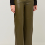 A person wearing olive green wide-leg faux leather pants, styled with a black long-sleeve top and brown leather ankle boots, against a light gray studio background.