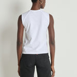 Person wearing a white sleeveless shirt and dark pants against a plain background