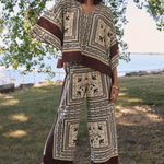 Woman wearing a patterned outfit standing outdoors with trees and water in the background