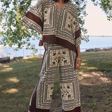 Woman wearing a patterned outfit standing outdoors with trees and water in the background