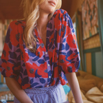 Woman in a colorful shirt holding a book in a room with a couch and decorative wall.