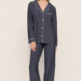 A woman modeling a two-piece pajama set with dark navy blue and white pinstripes, featuring a long-sleeve button-front top and matching wide-leg pants, set against a plain beige studio background.