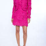 Person wearing a bright pink lace dress and jacket on a white background