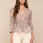 Woman wearing a floral blouse and white pants against a beige background