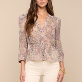 Woman wearing a floral blouse and white pants against a beige background