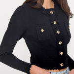 Black long-sleeve top with gold buttons worn by a person on a white background