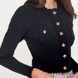 Black long-sleeve top with gold buttons worn by a person on a white background