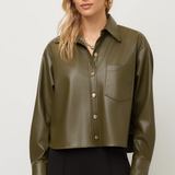 A woman modeling a cropped, long-sleeve olive green faux-leather button-up shirt with a chest pocket, paired with black pants, against a light gray studio background.
