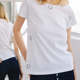 Woman wearing a white t-shirt with small logos, standing indoors.