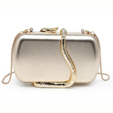 A metallic gold clutch bag with a textured snake-shaped strap draped over the front, set against a plain white background.