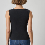 A woman viewed from the back wearing a sleeveless ribbed black top and blue jeans against a light gray studio background.
