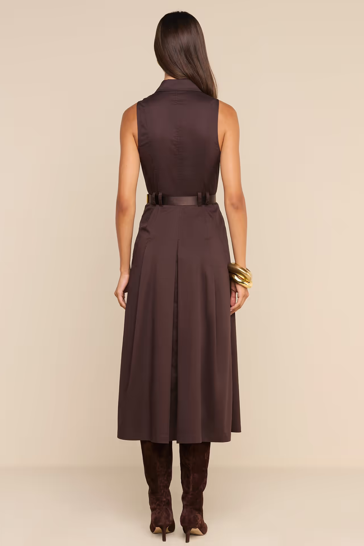 A woman shown from the back wearing a sleeveless dark brown midi dress with a matching belt, paired with dark brown boots, against a solid beige studio background.