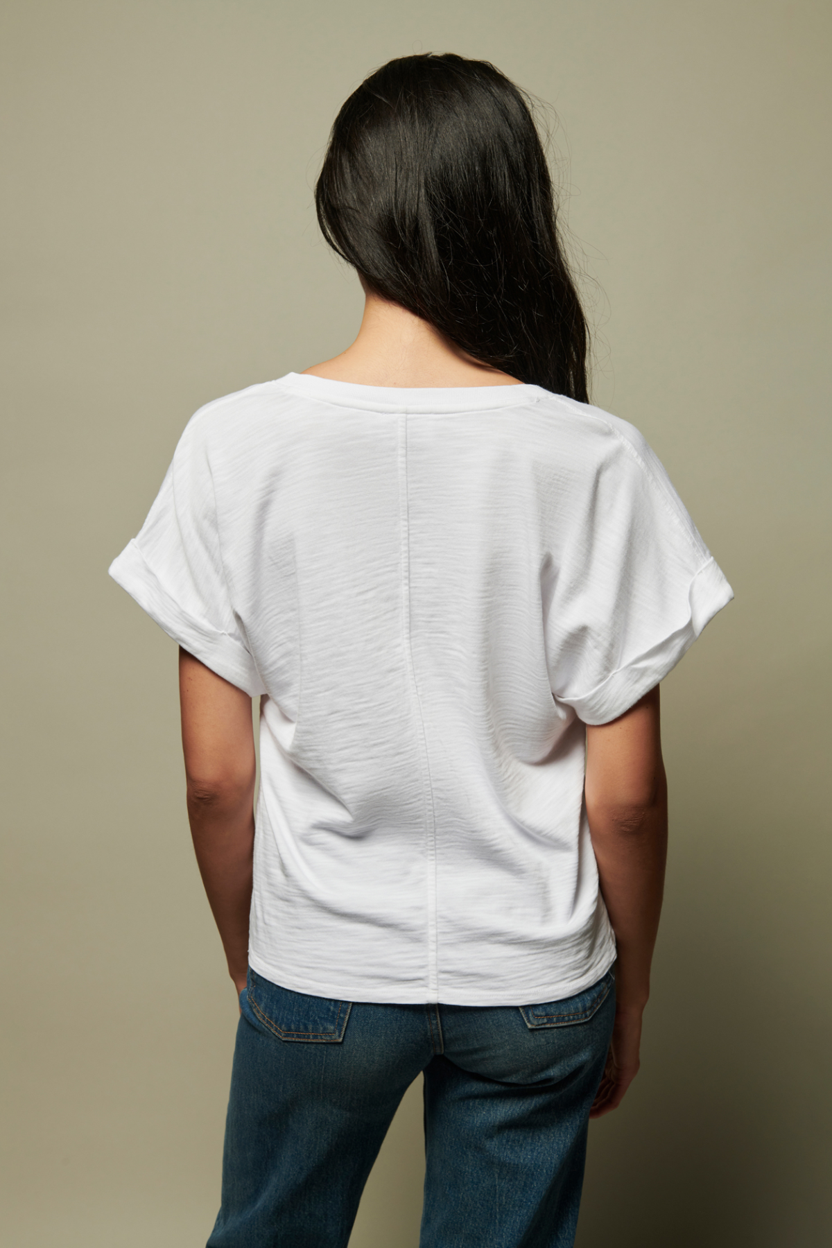 Person wearing a white t-shirt and blue jeans against a beige background