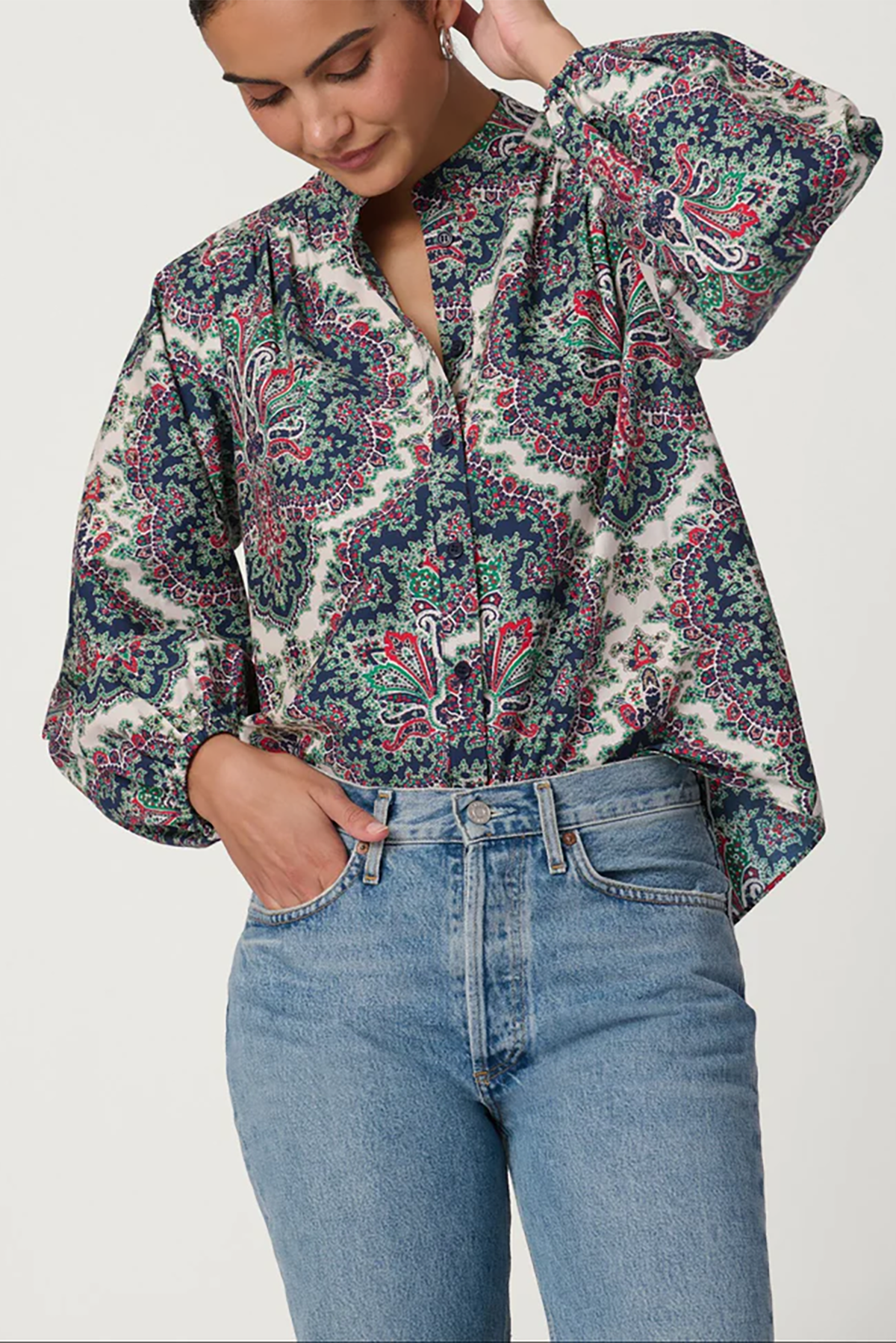 Woman wearing a patterned blouse and jeans on a white background