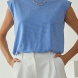 Woman wearing a blue sleeveless top and white pants against a plain background